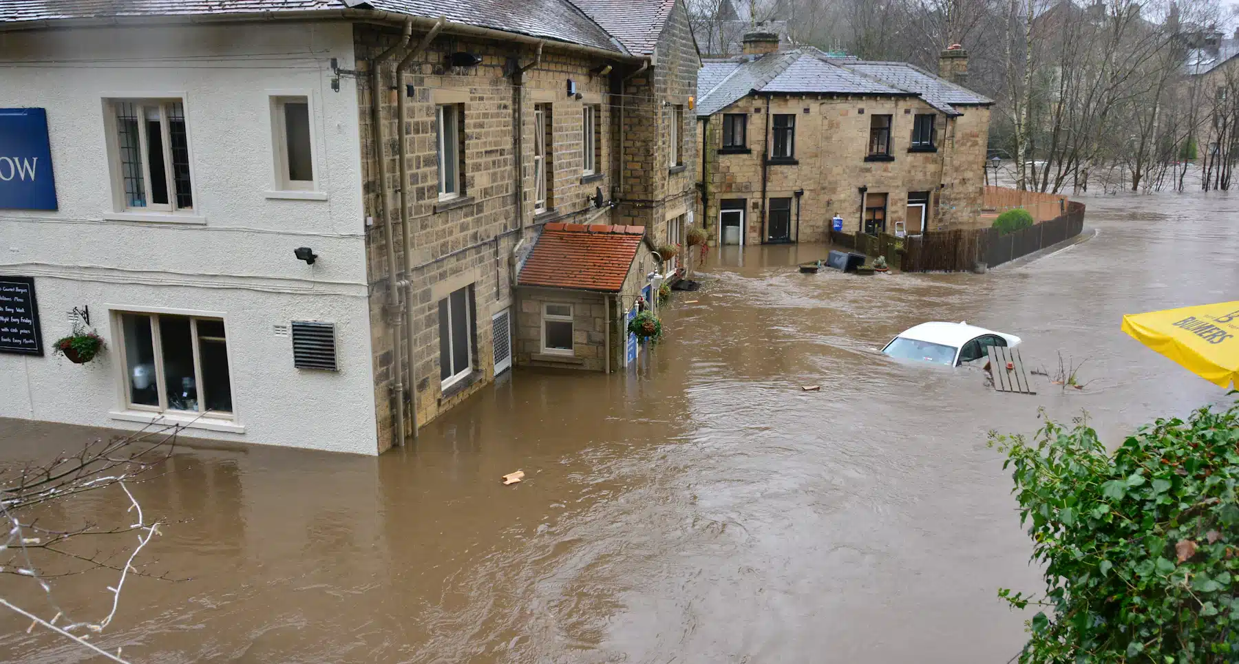 Flooded town with stone buildings Floodwater surrounding stone buildings and a partly submerged car in a town