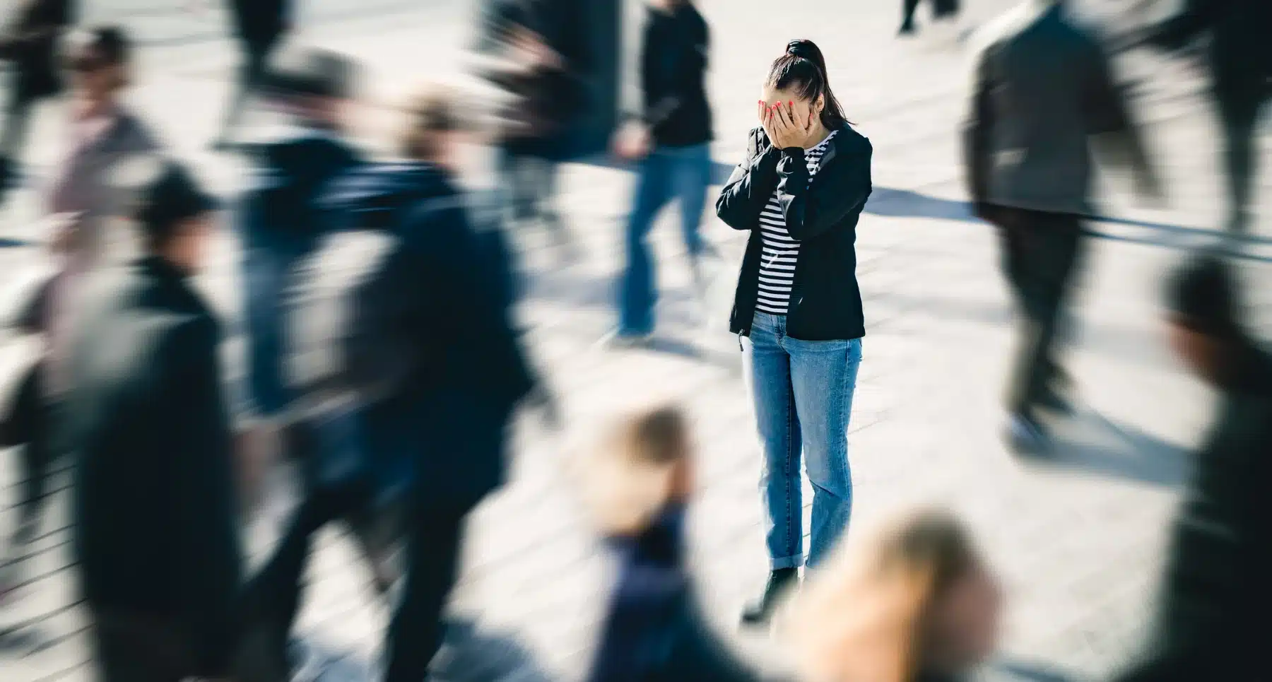 A woman covers her face with her hands as a blurred crowd moves past her