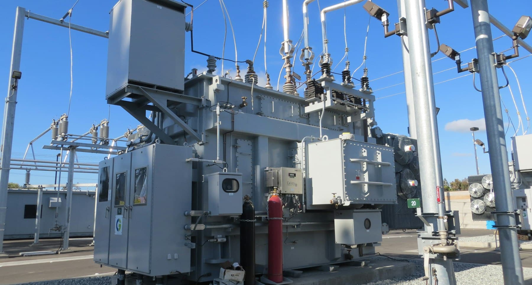 A large grey electrical transformer with pipes and cables in a power substation