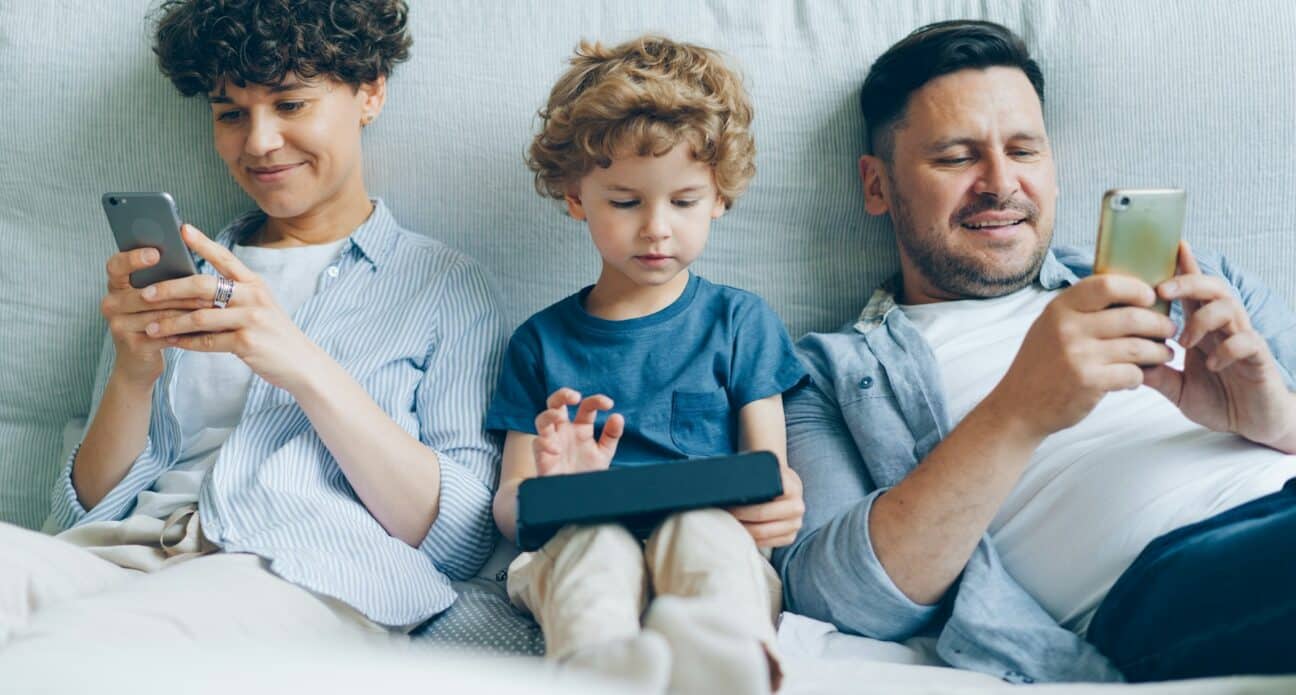 A man, woman and child sitting on a sofa, each looking at a mobile phone